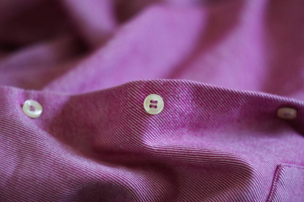 Detalhe de uma botão e uma camisa lilas.